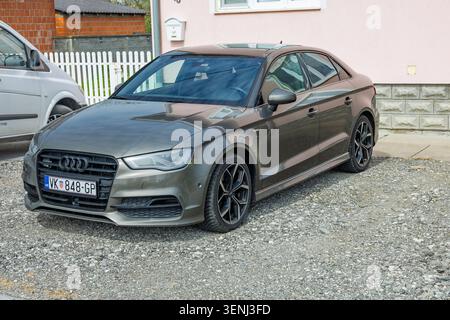 Vinkovci, Kroatien - 10. April 2026: Graue Audi Limousine parkt auf einer Schottereinfahrt neben einem rosafarbenen Haus und zeigt Leichtmetallfelgen, Kühlergrill und Reflexionen Stockfoto