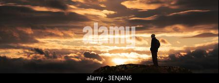 Silhouettenwanderer auf einem Berggipfel und genießen den Panoramablick auf einen majestätischen und dramatischen Sonnenuntergang mit orangefarbenen Wolken. Stockfoto