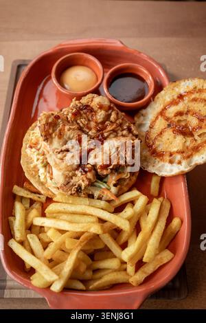 Köstliches gebratenes Hühnchen-Sandwich mit goldenen Pommes frites in rustikaler Umgebung Stockfoto
