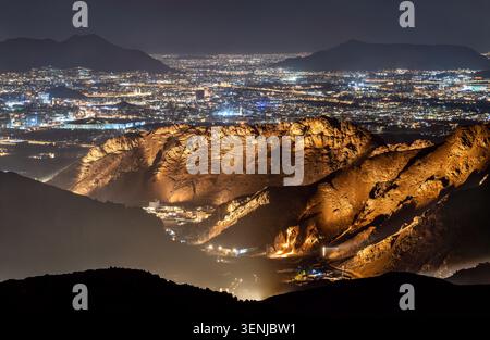 Ein Panoramablick bei Nacht vom Mount Uhud aus auf die beleuchtete Stadtlandschaft von Madinah mit zerklüfteten Bergkämmen im Vordergrund. Stockfoto