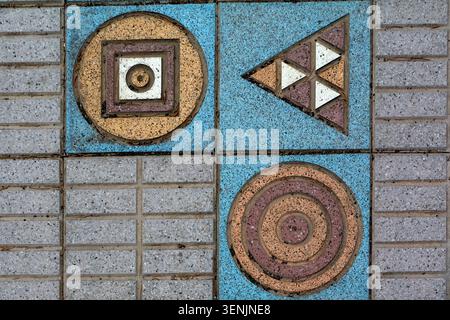 Eine Nahansicht einer geometrischen Anordnung von Pflasterfliesen zeigt farbenfrohe Einsätze von Kreisen, Quadraten und Dreiecken in Blau-, Ocker- und Stockfoto