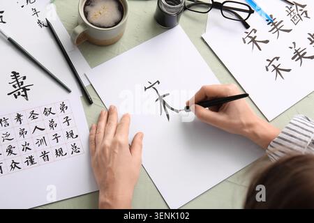 Person lernt traditionelle chinesische Kalligraphie mit Tinte und Pinsel auf weißem Papier, kulturelle Bildung und künstlerischen Ausdruck Stockfoto