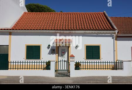 Traditionelles portugiesisches Haus mit gelben Zierleisten, grünen Fensterläden und einem lustigen Hundewarnschild in Coruche. Stockfoto