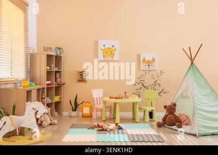 Helles Kinderspielzimmer mit Holzmöbeln, farbenfrohen Spielzeugen und dekorativen Wandbildern für die frühkindliche Entwicklung Stockfoto