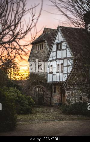 Ein altes Haus aus Stein und Fachwerk mit einem malerischen Garten und einem Bogengang, getaucht im warmen Glanz der untergehenden Sonne Stockfoto