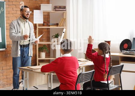 Musiklehrer leitet den Unterricht im Klassenzimmer, bei dem die Schüler die Hände heben, das Bildungsumfeld und der Lernprozess Stockfoto
