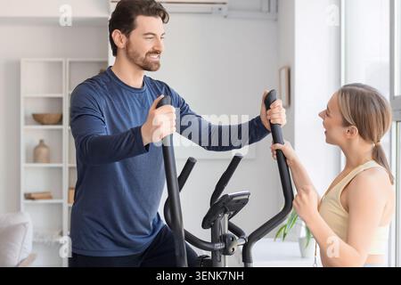 Glückliches Paar, das gemeinsam auf Crosstrainer zu Hause, Fitness und gesunde Lebensweise trainiert Stockfoto