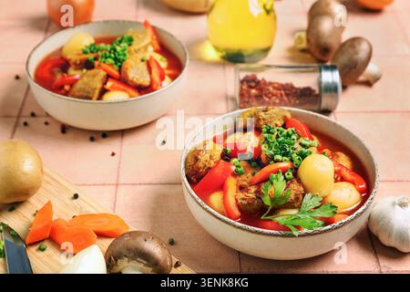 Herzhafter Rindereintopf mit Kartoffeln, roter Paprika und frischen Kräutern in Keramikschalen auf einem strukturierten Tisch Stockfoto