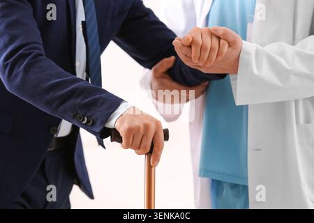 Älterer Mann in Anzug mit Stock unterstützt durch Arzt, medizinische Unterstützung und Seniorenbetreuung, professionelle medizinische Betreuung und die Bedeutung des Patienten Su Stockfoto