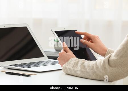 Frauenhände verwenden ein digitales Tablet und einen Laptop für Online-Geschäfte, Fernarbeit und E-Learning auf dem weißen Schreibtisch Stockfoto