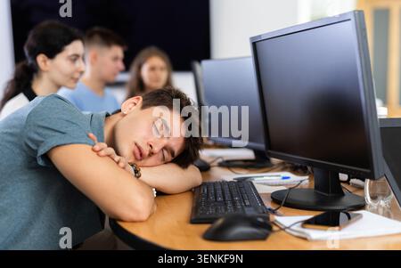 Erschöpfter junger Mitarbeiter, der sich mit der Softwareentwicklung beschäftigt und am Arbeitsplatz schläft Stockfoto