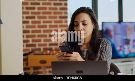 Lächelnde Person, die am Computertisch Benachrichtigungen über Mobiltelefone überprüft und eine Pause von der Arbeit einlegt. Stockfoto