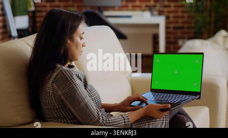 Person, die während der Arbeit von zu Hause aus E-Mails auf einem Laptop mit isoliertem Bildschirm liest. Indische Frau in gemütlicher, heller Wohnung, die Aufgaben erledigt, Geschäftsnachrichten auf Chroma Key Notizbuch liest. Stockfoto