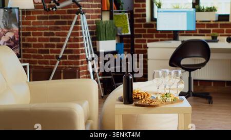 Charcuterie Board auf stilvollem Wohnzimmertisch neben einer Flasche teuren Wein. Leckere Gourmet Käseplatte und alkoholische Getränke Vorspeisen bereit, um von den Gästen der Appartementparty genossen zu werden. Stockfoto