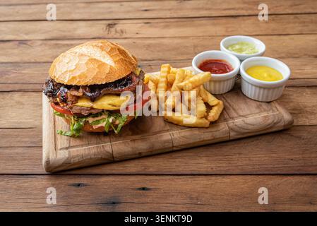 Burger-Komposition mit Rindfleisch, Käse, Speck und Tomaten. Pommes Frites und Saucen zum Tauchen komplettieren die Sicht. Bei Aufnahmen mit hohem Winkel werden kräftige Farben und Texturen hervorgehoben Stockfoto