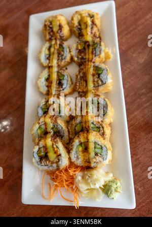 Hochwinkel-Nahaufnahme knuspriger, frittierter Tempura-Sushi-Brötchen auf einer weißen rechteckigen Platte. Die Brötchen werden mit herzhafter Soße und Serv getränkt Stockfoto