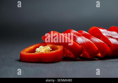 Saubere Komposition aus geschnittenem rotem Chilischoten in einer ordentlichen Reihe vor dunkelgrauem Hintergrund Stockfoto
