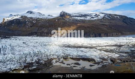 Der Svinafellsjokull-Gletscher bricht auseinander, während er zu einem schlammigen Wasserkörper schmilzt. Eisberge schweben im Wasser, während felsiges Land die Szene umgibt. Der Bereich Stockfoto