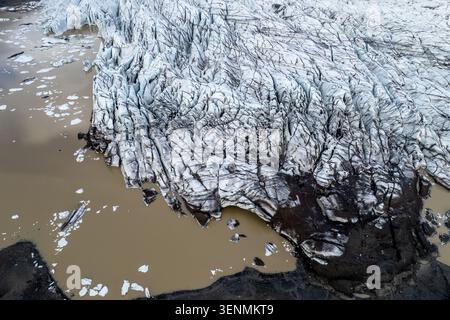 Der Svinafellsjokull-Gletscher bricht auseinander, während er zu einem schlammigen Wasserkörper schmilzt. Eisberge schweben im Wasser, während felsiges Land die Szene umgibt. Der Bereich Stockfoto