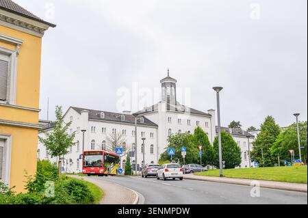 Iserlohn, Deutschland - 05. Juni 2026: Straßenblick mit rotem öffentlichem Bus vorbei an historischem Gebäude unter bewölktem Himmel. Stockfoto