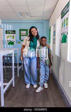 Frau und Kind stehen zusammen im Klassenzimmer in der Nähe von Recyclingplakaten, Kind trägt Rucksack Stockfoto