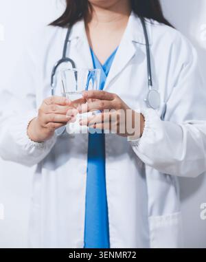 Porträt einer asiatischen Ärztin, die eine Kaffeetasse auf weißem Atelierhintergrund hält Stockfoto