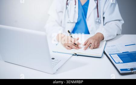 Ärztin mittleren Alters, die auf dem Laptop im Arztzimmer arbeitet Stockfoto