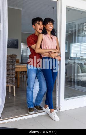 Verschiedene Paare kommen durch die Schiebetür, nachdem sie nach Hause zurückgekehrt sind, Mann umarmt Frau während sie lacht Stockfoto