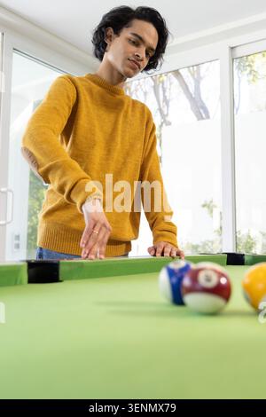 Asiatischer Mann mit Senfpullover am grünen Billardtisch, der zu Bällen greift und einen Ring zeigt Stockfoto