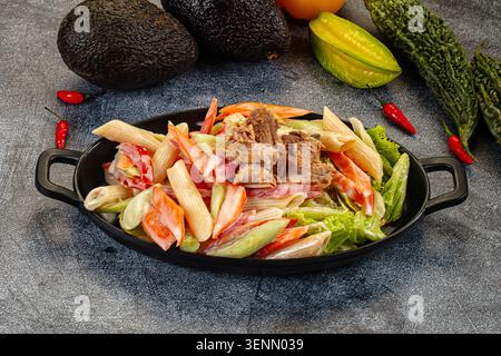 Appetitlicher Nudelsalat mit Thunfisch und Gemüse in einer cremigen Sauce. Die Top-Down-Ansicht auf dunklem Hintergrund hebt frische rote, grüne und beige Farben hervor. P Stockfoto