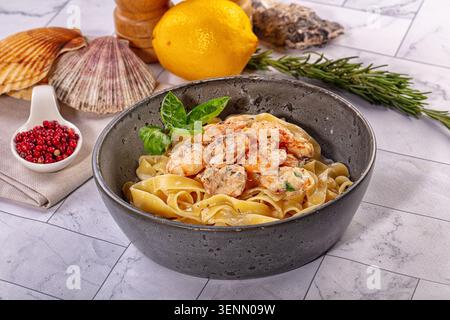Köstliche Fettuccine-Pasta mit gegrillten Garnelen in cremiger Sauce. Garniert mit Basilikum in dunkler Schüssel. Zutaten wie Zitrone, Rosmarin und Muscheln aus Meeresfrüchten Stockfoto