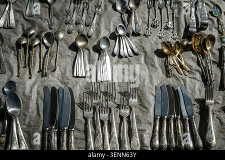 Eine große Sammlung von antiken und Vintage-Besteck, einschließlich Gabeln, Löffeln und Messern, ist sorgfältig auf einer grauen Stoffoberfläche angeordnet. Die kunstvollen s Stockfoto