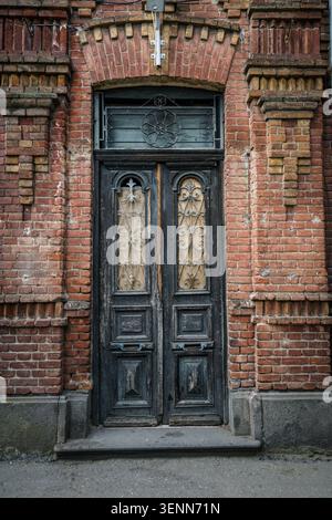 Eine alte und rustikale dunkelblaue Holztür mit komplizierten schmiedeeisernen Gittern steht in einer verwitterten roten Ziegelfassade. Das historische Zentrum Stockfoto