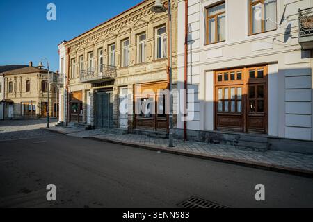 Eine ruhige Straßenszene in Gori, Georgia, zeigt historische mehrstöckige Gebäude mit kunstvollen klassischen Fassaden, Balkonen und traditionellem Holzdach Stockfoto
