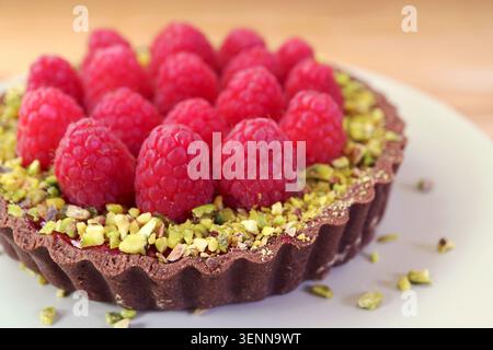 Schließen Sie eine komplette runde Himbeertorte mit Pistazien und Schokoladenkruste Stockfoto