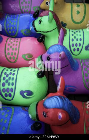 Diese Nahaufnahme zeigt einen lebendigen Stapel aufblasbarer Spielzeugpferde in verschiedenen Farben wie Pink, Grün, Lila und Blau. Die Spielzeuge, die vielleicht bei gefunden wurden Stockfoto