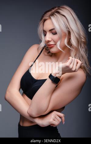 Eine junge Frau mit blondem Haar, die einen schwarzen Sport-BH und Smartwatch trägt Stockfoto