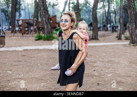 Happy Woman gibt einem Kleinkind einen Huckepack-Ritt im Freien Stockfoto