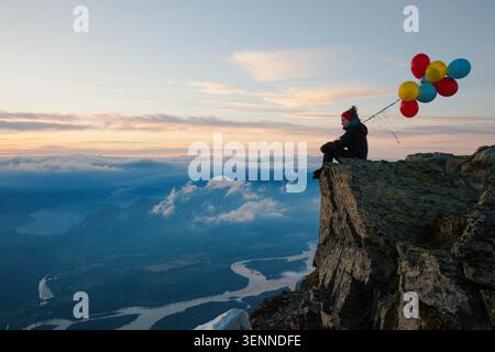 Der Wanderer sitzt mit bunten Ballons auf einem Berggipfel Stockfoto