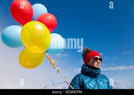Frau in Winterkleidung hält bunte Ballons vor blauem Himmel Stockfoto