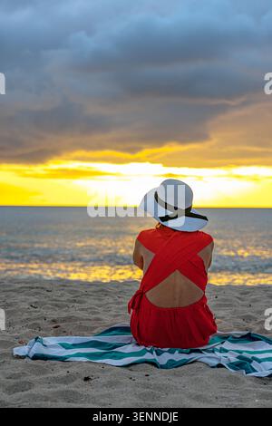 Frau mit Hut, die den Sonnenuntergang am Strand beobachtet Stockfoto