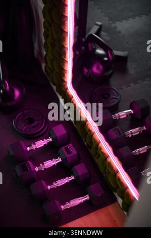 Heim-Fitnessgeräte mit Kurzhanteln und Wasserhanteln, beleuchtet durch Neon Stockfoto
