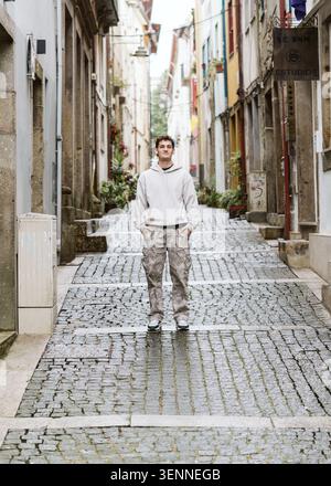 Junger Mann, der auf einer nassen Kopfsteinpflasterallee steht Stockfoto