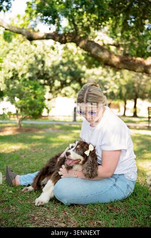 Frau kuschelt Seniorenspaniel auf Gras unter einem Schatten spendenden Baum Stockfoto