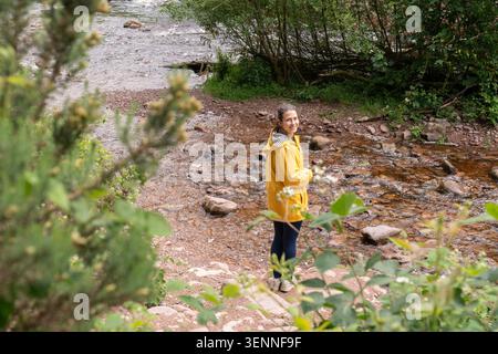 Frau mit gelbem Regenmantel lächelt am Fluss Stockfoto