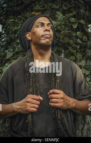 Ein nachdenklicher Mann mit Dreadlocks, der an der Efeuwand steht Stockfoto