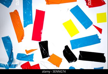 Gerissene Klebebandstücke in hellen Farben sind auf einer weißen Oberfläche verstreut und haben verschiedene Formen und Größen für künstlerische Anwendungen Stockfoto