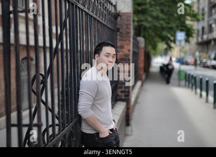 Junger asiatischer Mann, der sich an einen Zaun auf einer Stadtstraße lehnt Stockfoto