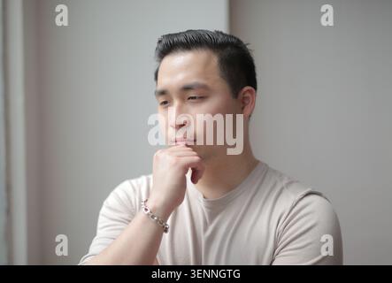 Nachdenklicher junger asiatischer Mann mit Hand am Kinn Stockfoto