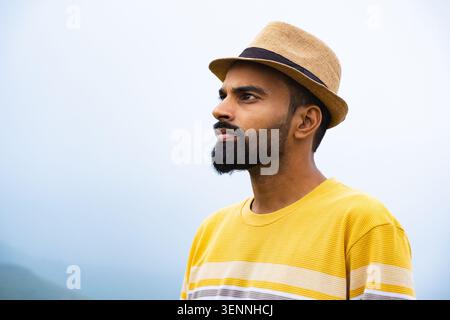 Ein Mann mit Bart und Fedorahut blickt nachdenklich in die Ferne draußen. Stockfoto